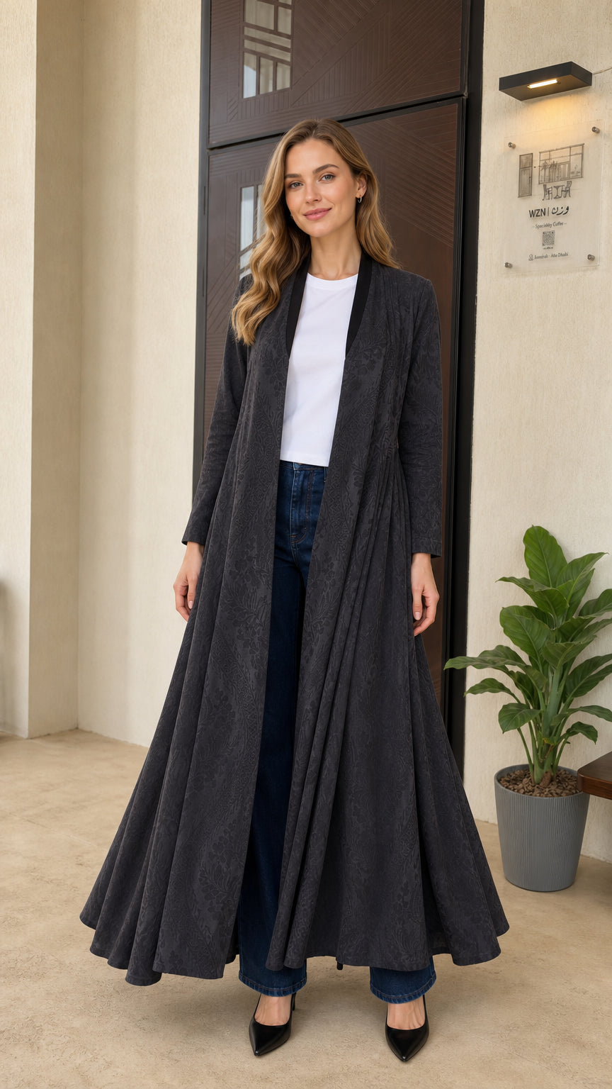 Front full-length view of woman wearing charcoal grey pleated maxi duster coat with white top and jeans