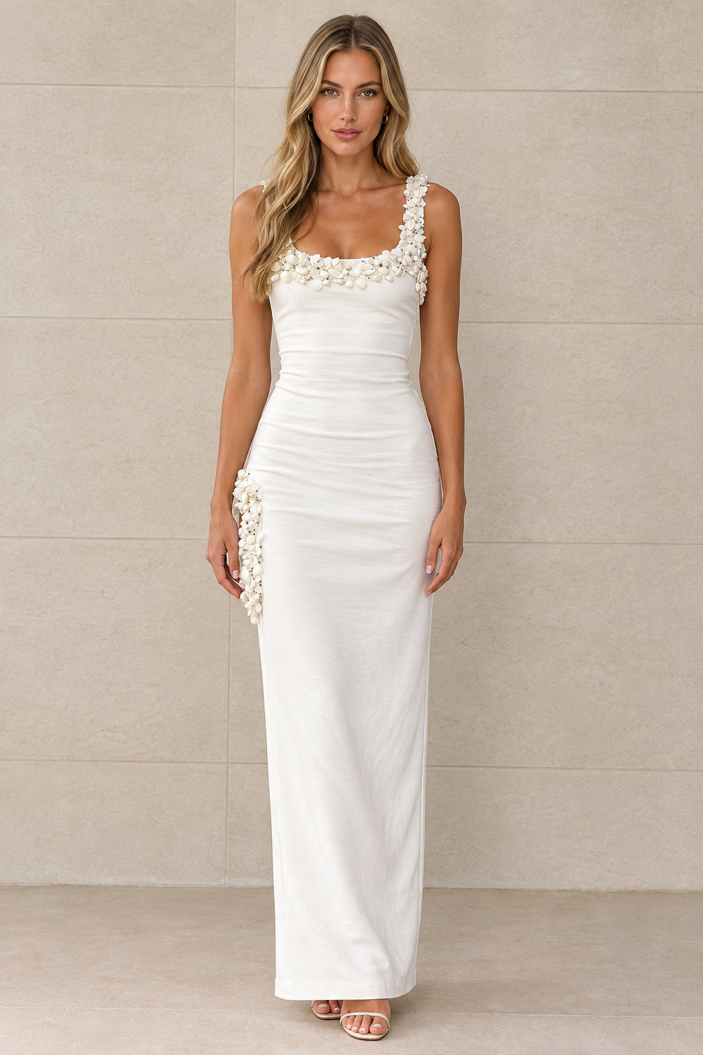 Front view of model wearing white sleeveless maxi dress with 3D floral neckline and hip accents
