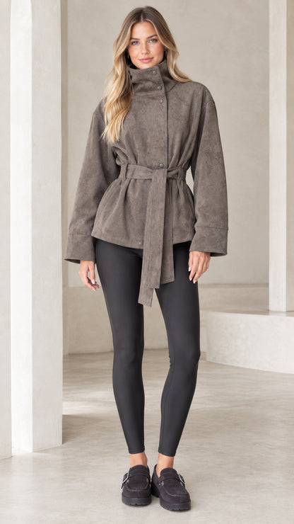 Front view of model wearing taupe high-neck belted faux suede jacket with black leggings