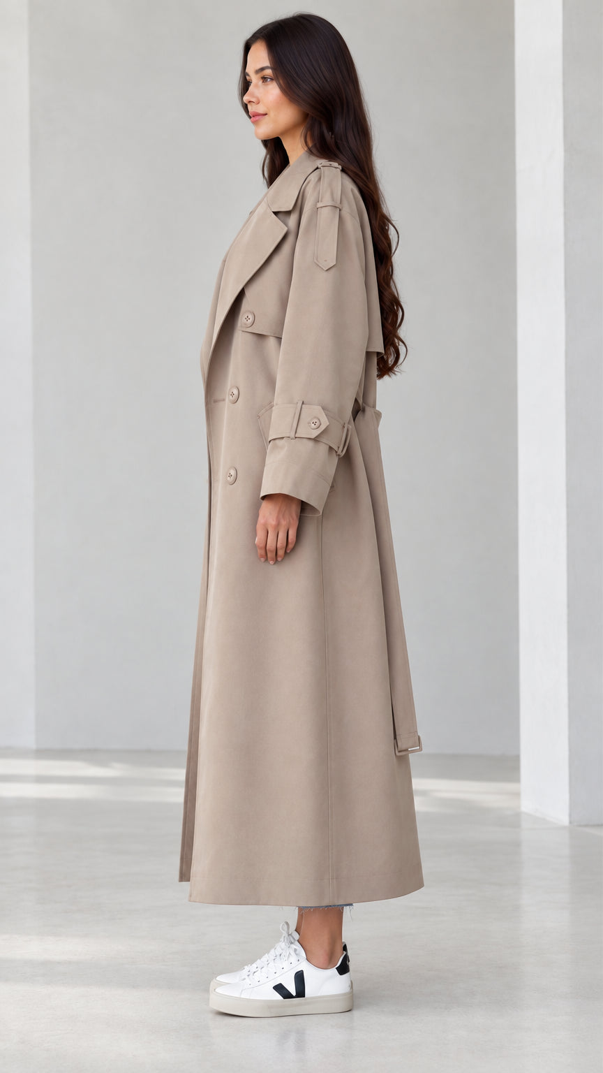 Side profile view of women's beige maxi trench coat showing sleeve straps and fluid drape