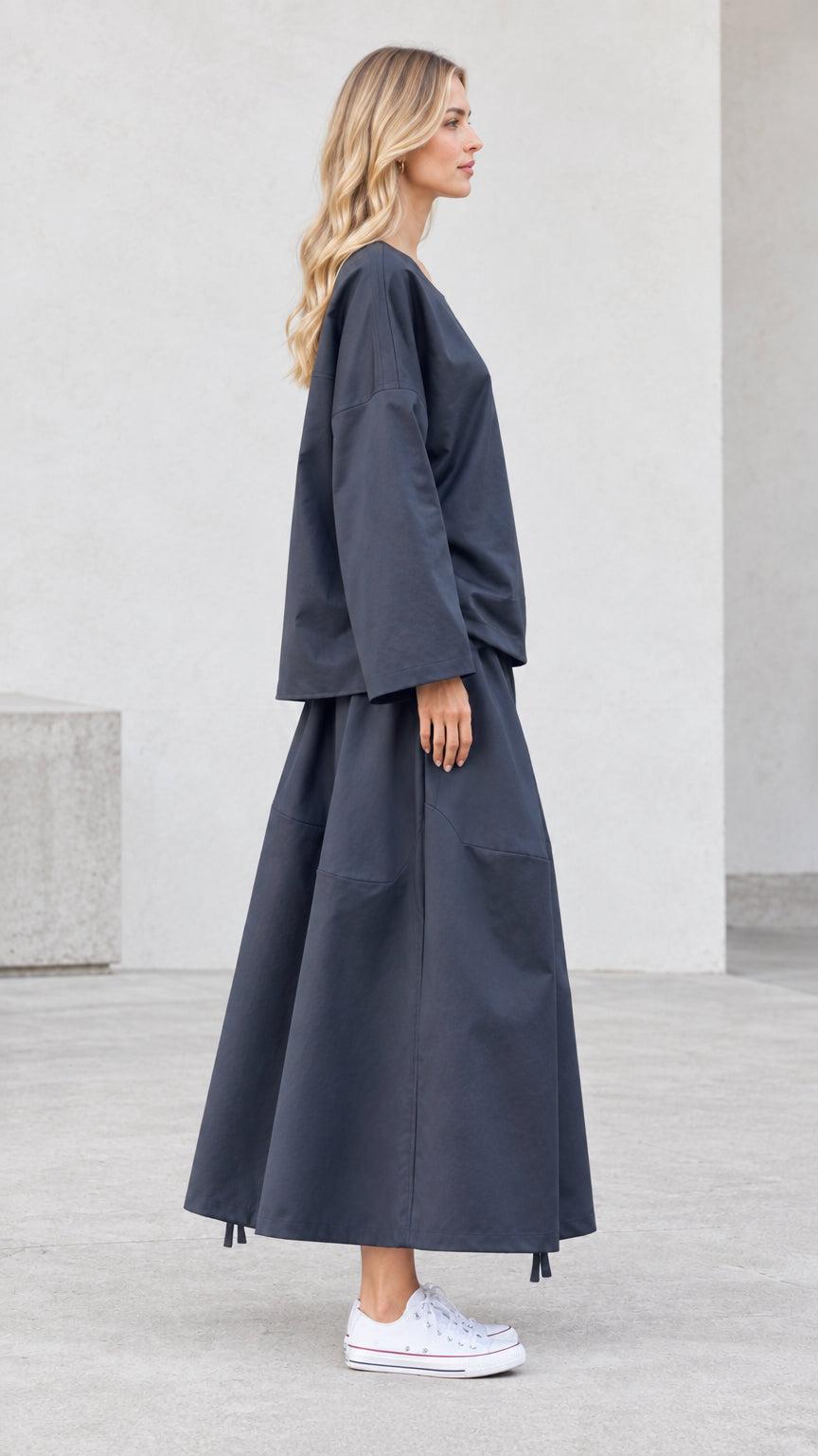 Side view of model wearing charcoal grey matching skirt and top set with white sneakers