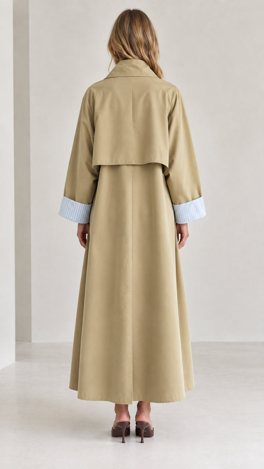 Back view of woman wearing long khaki trench coat featuring classic back storm flap