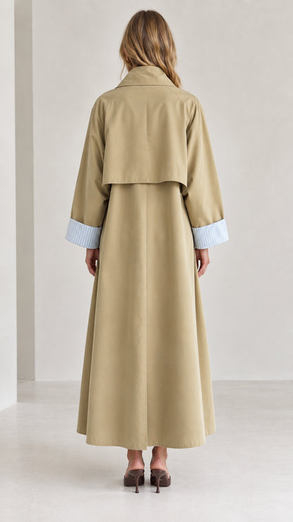Back view of woman wearing long khaki trench coat featuring classic back storm flap