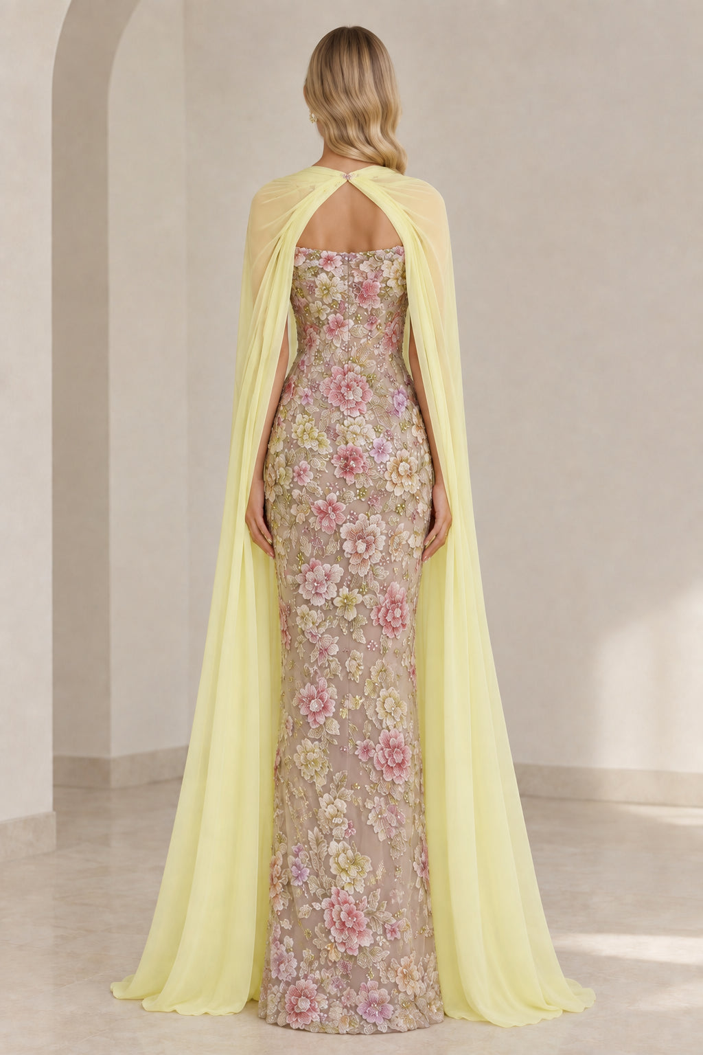 Back view of model showing keyhole cutout chiffon cape and floral lace column dress