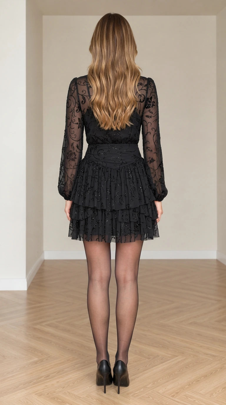 Back full view of woman in Black sheer long sleeve tiered ruffle mini dress