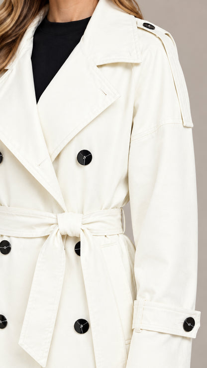 Close-up detail of white trench coat showing lapel, shoulder epaulette, and buttons