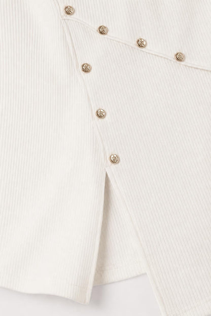 Close-up detail of gold-tone buttons and side hem slit on white dress