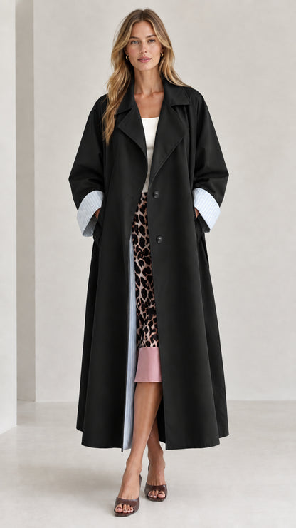 Front view of woman wearing black long trench coat with striped cuff detail