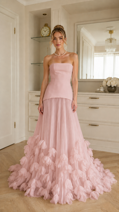Front view of blush pink strapless evening gown with flowing pleats and ruffle hem