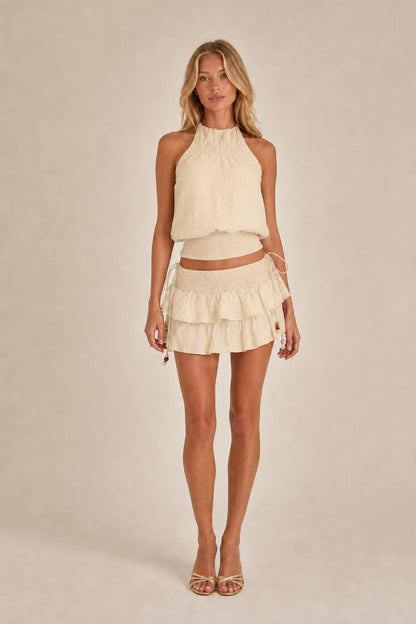Model wearing beige halter top and ruffled mini skirt set